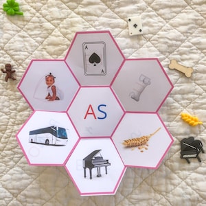May include: A hexagonal educational card featuring the letters AS in the centre, surrounded by six smaller hexagons displaying images of an ace of spades card, a bone, a stalk of wheat, a grand piano, a bus, and a child playing with a jump rope.