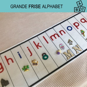 May include: A white fabric strip with the letters of the alphabet printed in red and blue. The letters are arranged in order from g to p. There are various small toys and objects attached to the strip, including a toy car, a palm tree, a weight, a jellyfish, a birdhouse, and wooden letters M and N.