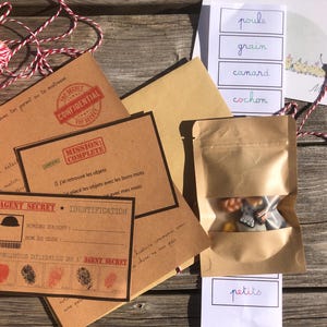 Puede incluir: Un kit de actividades con temática de agente secreto que incluye sobres de papel marrón, una tarjeta de misión cumplida, una tarjeta de identificación de agente con espacios para huellas dactilares, una bolsa con figuras y tarjetas de palabras.