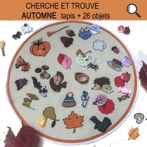 Peut inclure: Un ensemble d'objets décoratifs sur le thème de l'automne, dont une citrouille, des feuilles et un hérisson, disposés sur un tapis circulaire beige. Le texte "CHERCHE ET TROUVE AUTOMNE tapis + 26 objets" est en haut. Les objets sont colorés et fantaisistes.