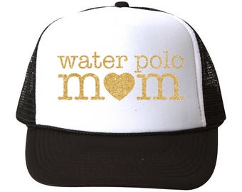 May include: A white and black trucker hat with a black mesh back. The front of the hat has gold glitter lettering that says "water polo mom" with a gold glitter heart.