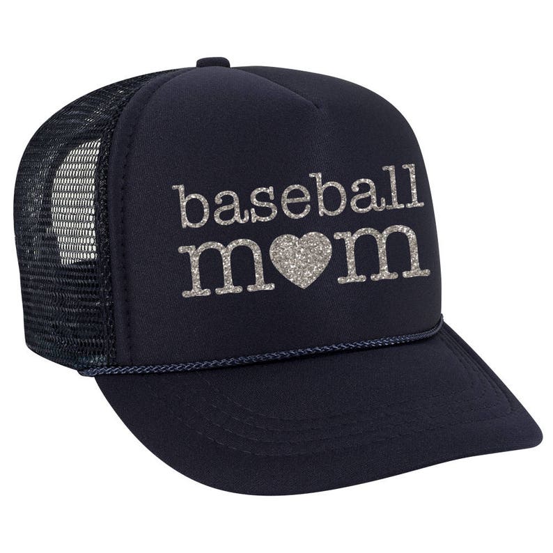 May include: A navy blue trucker hat with a black mesh back. The hat has a silver glitter design that says "baseball mom" with a heart in the middle.