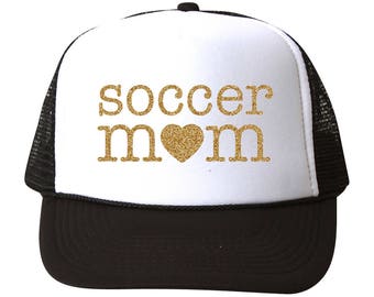 May include: White and black trucker hat with a gold glitter design that says "Soccer Mom" with a heart in the middle.