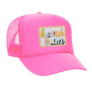 May include: Bright pink trucker hat with a mesh back and a curved brim. The front of the hat features a rectangular patch with the words "beach bum" in colorful, embroidered lettering. A fun, casual accessory.