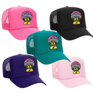 May include: Five trucker hats with a mesh back. The hats are in pink, black, teal, purple, and light pink. Each hat has an embroidered patch of a UFO with the text "Get in Loser" underneath.