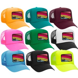 May include: Ten trucker hats in various colors with a rainbow and "RAD" patch on the front. The hats are in the following colors: yellow, teal, maroon, pink, green, white, black, blue, and neon yellow.