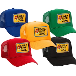 May include: Five trucker hats in different colors with a flower and the text "HAVE A NICE DAY" embroidered on the front.