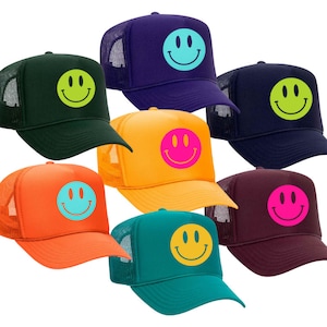 May include: Seven trucker hats with a mesh back. Each hat features a different colored smiley face on the front. The smiley faces are yellow, green, blue, pink, orange, and red.