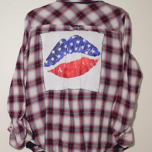 Może przedstawiać: Koszula flanelowa w kratę czerwoną i niebieską z białą łatą z tyłu, przedstawiającą czerwony i niebieski wzór ust z białymi gwiazdami.