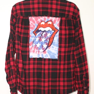Puede incluir: Camisa de franela a cuadros rojos y negros con un parche tie-dye con el logotipo de la lengua de los Rolling Stones en la espalda.