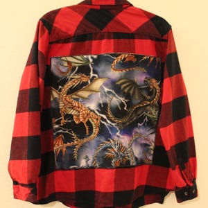 Może przedstawiać: Flanelowa koszula w kratę czerwoną i czarną z naszywką z nadrukiem smoka na plecach. Naszywka przedstawia wiele smoków z błyskawicami w tle.