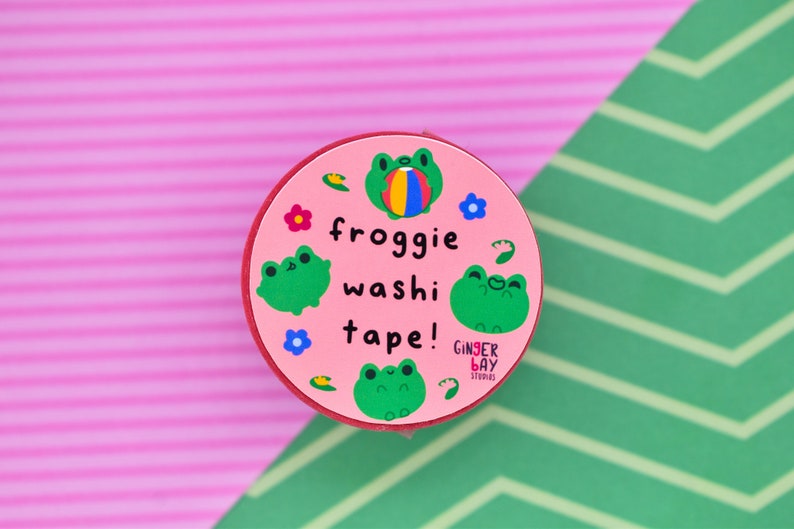 May include: Pink round washi tape dispenser with a frog design. The dispenser has the text "froggy washi tape!" and a small logo that says "Ginger Bay Studios".