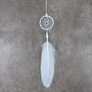 May include: A white dreamcatcher featuring a circular web design, small beads, and a large, fluffy feather. The dreamcatcher hangs from a thin white string against a grey background. This decorative item is often used for home decor.