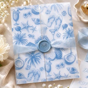 May include: A translucent vellum gatefold invitation wrap featuring a blue tropical pattern of palm trees, seashells, flip-flops, pineapples, and cocktails. The wrap is secured with a light blue silk ribbon and a circular wax seal with a palm tree.