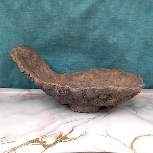 May include: A handcrafted, brown, organic-shaped bowl with a textured surface. The bowl has a unique, asymmetrical design, perfect for decorative use or as a centerpiece. The bowl is made of a natural material, adding a rustic touch to any space.