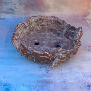 Könnte beinhalten: Ein handgefertigter, rustikaler Bonsai-Topf mit strukturiertem, organischem Design. Der braun-beige Keramiktopf hat zwei Abzugslöcher und eine einzigartige, unregelmäßige Form, ideal für Miniaturbäume.