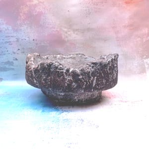 Peut inclure: Un bol circulaire brun foncé avec une surface extérieure rugueuse, inégale et texturée. Le bord du bol est dentelé et irrégulier, présentant un centre creux profond avec une base large qui se rétrécit légèrement vers le bas.