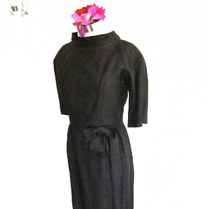 May include: A black dress with a bow at the waist. The dress has a simple, elegant design and is made of a smooth, textured fabric.