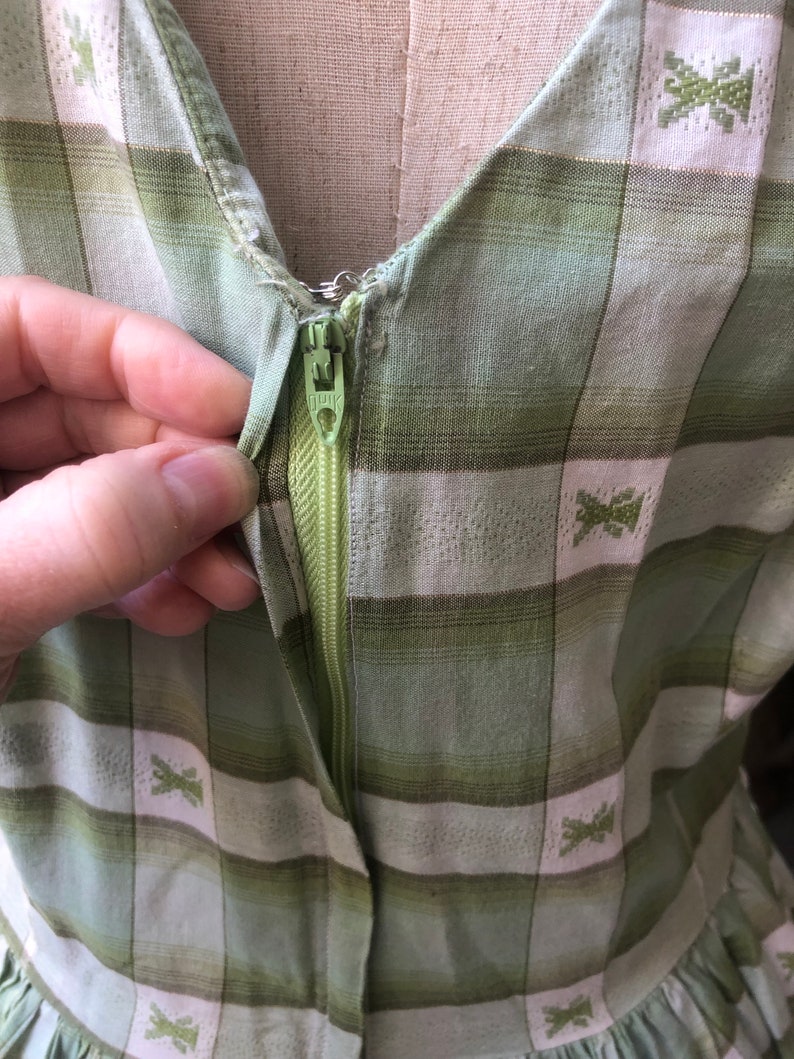 Op de afbeelding: Een groene en witte geruite jurk met een rits. De jurk heeft een klein geborduurd ontwerp op de stof.
