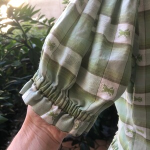 Op de afbeelding: Een groene en witte geruite jurk met een geplooide mouwdetail. De jurk heeft een wit geborduurd patroon over de hele oppervlakte.