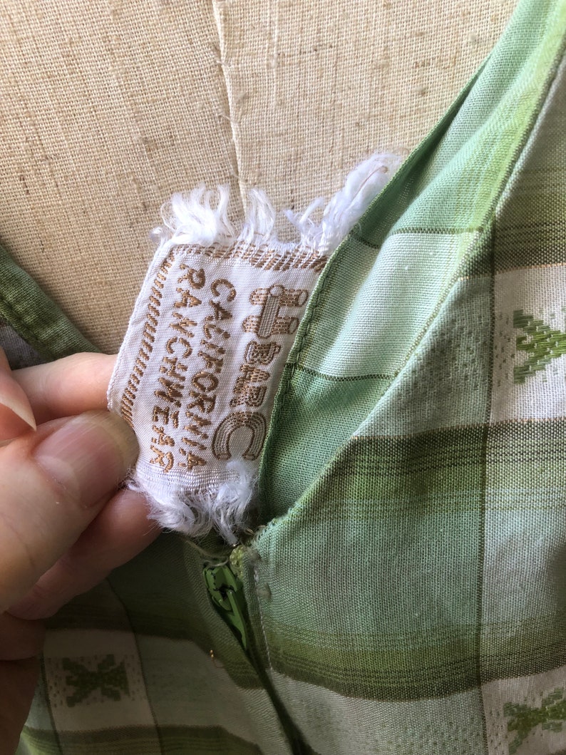 Op de afbeelding: Een groene en witte geruite jurk met een rits en een label met de tekst "California Ranchwear" in bruine letters.