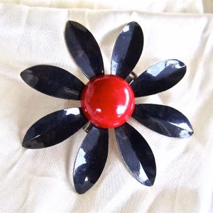May include: A black and red flower brooch with a red center and six black petals.