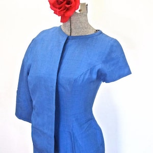 May include: A blue dress with a long, flowing sash. The dress has a fitted bodice and a full skirt. A red rose is pinned to the dress.