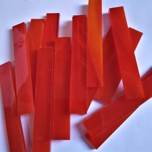May include: A collection of rectangular, translucent, red-orange glass pieces. The pieces are of varying lengths and widths, with a glossy finish. The arrangement is scattered, with some pieces overlapping. The color gradient ranges from a deep red to a bright orange.