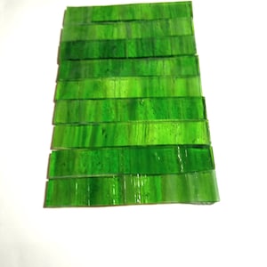 May include: A stack of rectangular, transparent, green glass tiles. The tiles are arranged in a slightly fanned-out pattern, showcasing varying shades of green. The glass has a glossy finish, reflecting light and creating a vibrant appearance.