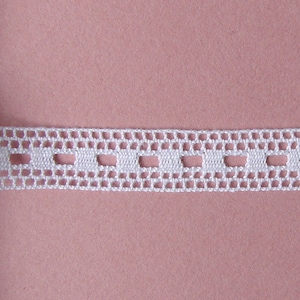 May include: White crochet trim with a repeating pattern of small squares. The trim is rolled up and partially unrolled, showing the pattern.