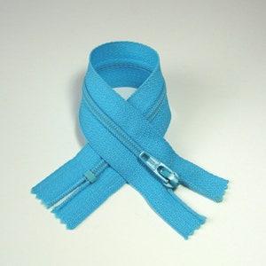 May include: A light blue zipper with a silver slider. The zipper is folded in half and tied in a knot.