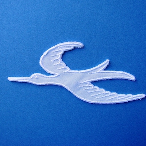 May include: White embroidered bird applique in a flying pose on a blue background.