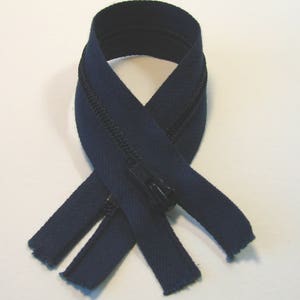 May include: A navy blue zipper with a black slider. The zipper is folded in half and the ends are frayed.