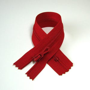 May include: A red zipper with a red slider. The zipper is folded in half and the slider is in the middle.