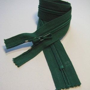 May include: A green zipper with a metal slider. The zipper is folded in half and the slider is in the middle of the zipper.