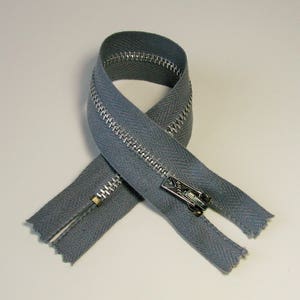 May include: A gray zipper with silver metal teeth and a matching pull tab. The zipper is looped in a figure-eight shape, showcasing its construction and design. The zipper is made of a durable fabric.