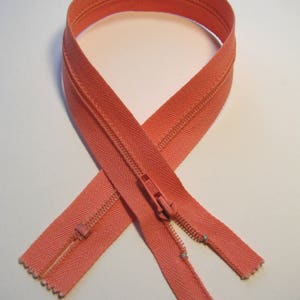 May include: A coral colored zipper with a metal slider. The zipper is open and the two sides are laying flat.