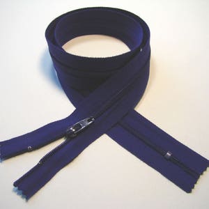 May include: A navy blue zipper, coiled and laid out on a white surface. The zipper is open, revealing the metal teeth and slider. The fabric tape is a solid, dark blue color.