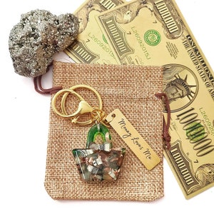 May include: A gold keychain with a green shopping bag charm filled with fake money and a tag that says "Money Loves Me". The keychain is in a hessian bag with two gold £1,000,000 notes.