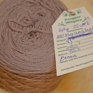 Może przedstawiać: Motka brązowej przędzy wełnianej merino 2-nitkowej z etykietą z napisem "Frogger Niagara 2ply. 25 WPI 100% Wełna Merino Skład Waga: 27g Gramy: 2,7 Uncje: 550 Yardy: 502 Metry: Brązowy Dziękujemy za zakup recyklingu! Instagram TheFrogger Niagara"