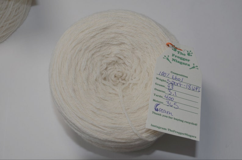 May include: A skein of cream-colored wool yarn, labeled as 100% wool, Sport weight, 18 WPI. The label also includes the weight in grams (93), ounces (3.1), yards (400), and meters (365).