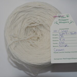 May include: A skein of cream-colored wool yarn labeled "The Frogger Niagara" with details about the yarn: 100% wool, Sport weight, 134 grams, 4.4 ounces, 550 yards, 502 meters.