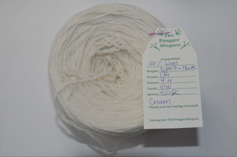 May include: A skein of cream-colored wool yarn labeled "The Frogger Niagara" with details about the yarn: 100% wool, Sport weight, 134 grams, 4.4 ounces, 550 yards, 502 meters.