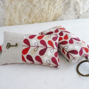 May include: Two keychains with a red, white, and brown floral pattern. One keychain has a small key attached to it.