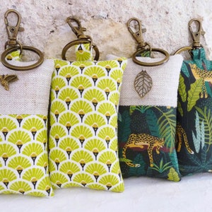 May include: Four keychains with different fabric designs. The keychains are made of linen and feature a variety of patterns, including a geometric design, a jungle scene, and a floral pattern. Each keychain has a brass ring and a metal charm.