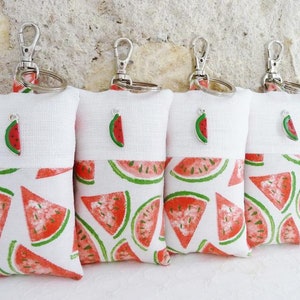 May include: Four white fabric keychains with a watermelon print and a small watermelon charm. The keychains are attached to silver key rings.