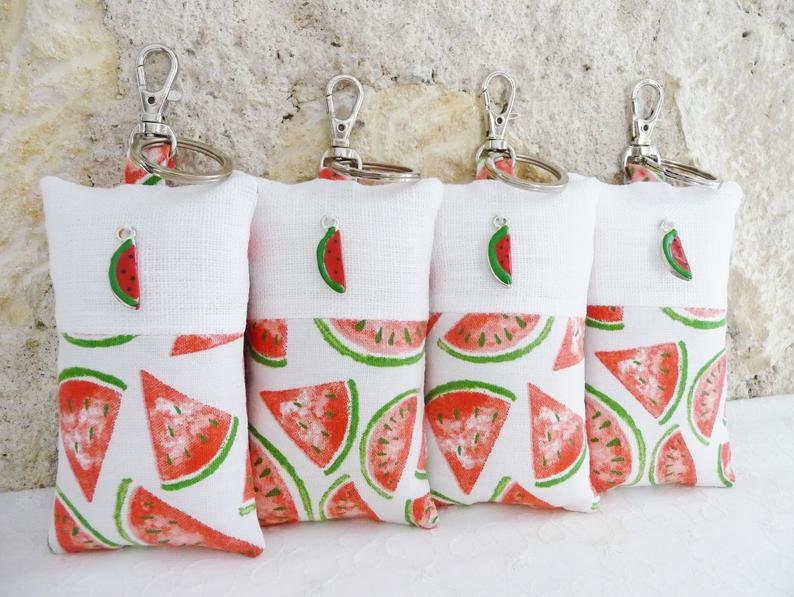 May include: Four white fabric keychains with a watermelon print and a small watermelon charm. The keychains are attached to silver key rings.