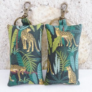 May include: Two green and brown fabric keychains with a leopard print design. Each keychain has a gold metal ring and a gold metal clasp.