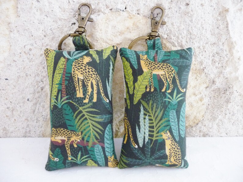 May include: Two green and brown fabric keychains with a leopard print design. Each keychain has a gold metal ring and a gold metal clasp.