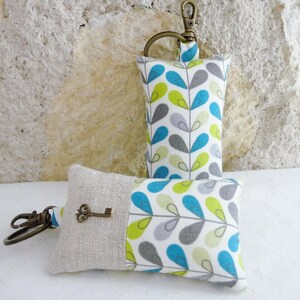 May include: Two keychains with a fabric design of teal, green, and gray leaves on a white background. One keychain has a key attached to it.